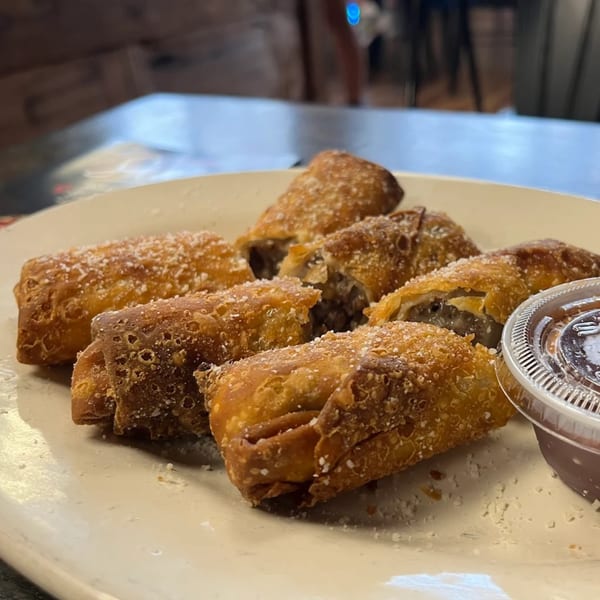 Crispy, golden-brown egg rolls, some cut open to reveal a savory filling, dusted with Parmesan cheese.