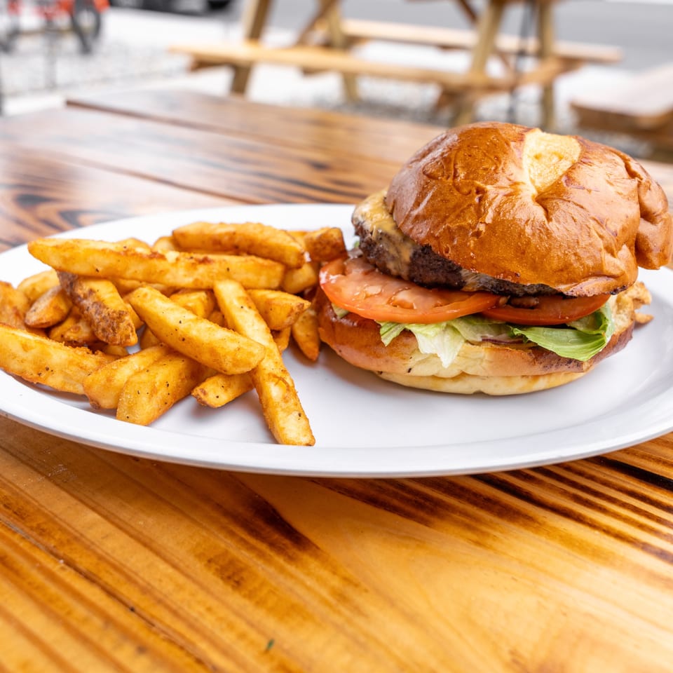 A cheeseburger with lettuce and tomato, served with a side of seasoned fries on a white plate.