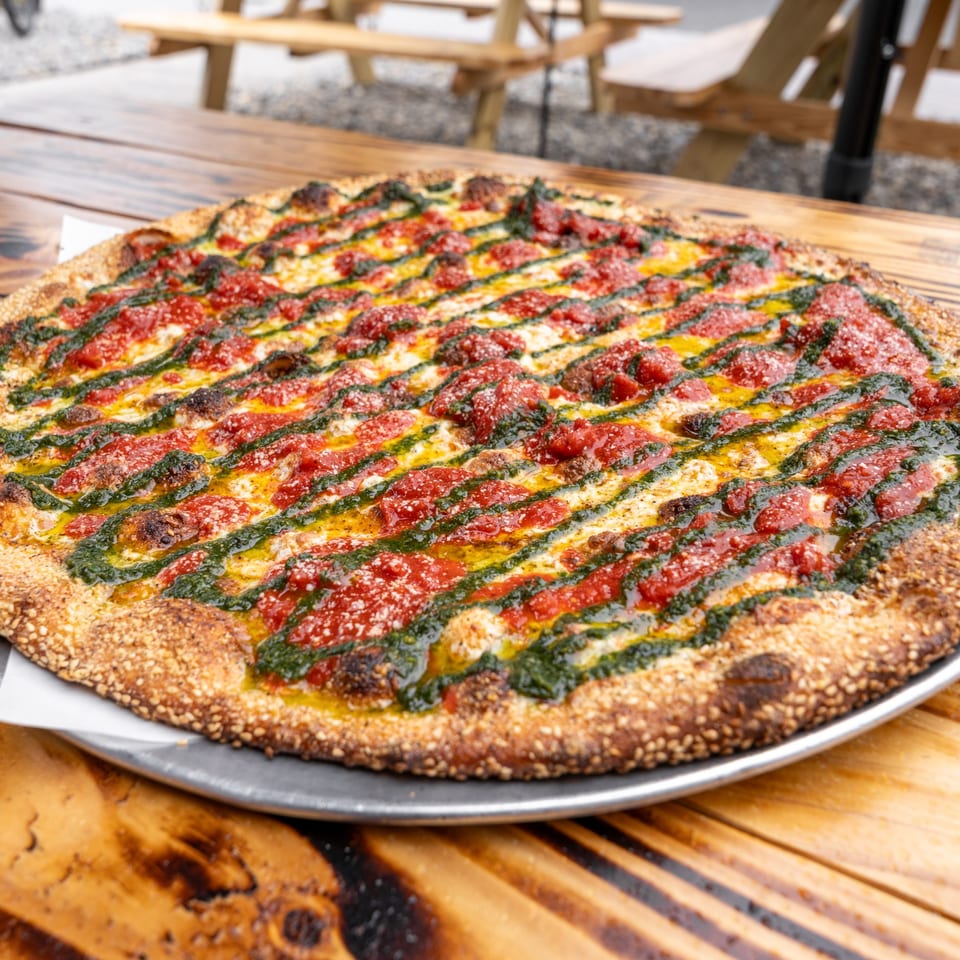 The Sauce Pizzeria's pizza with red sauce, pesto, and cheese, on a wooden table.