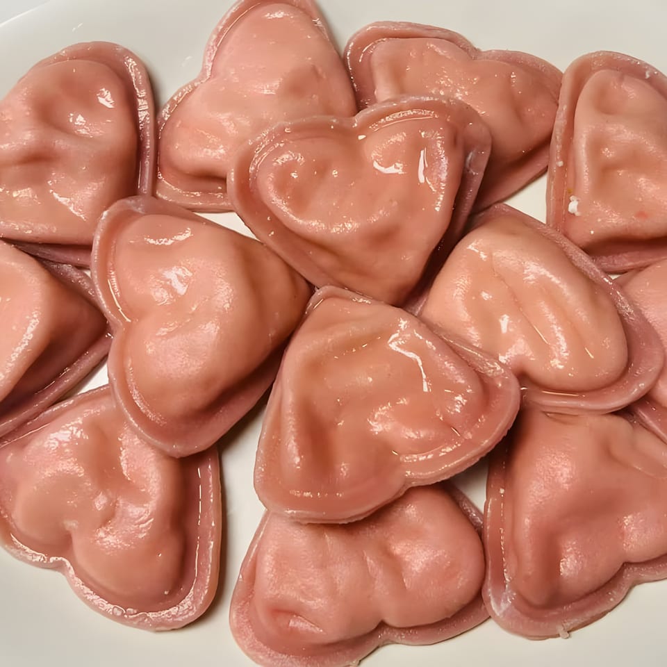 Close-up of heart-shaped pink ravioli or dumplings on a white plate.