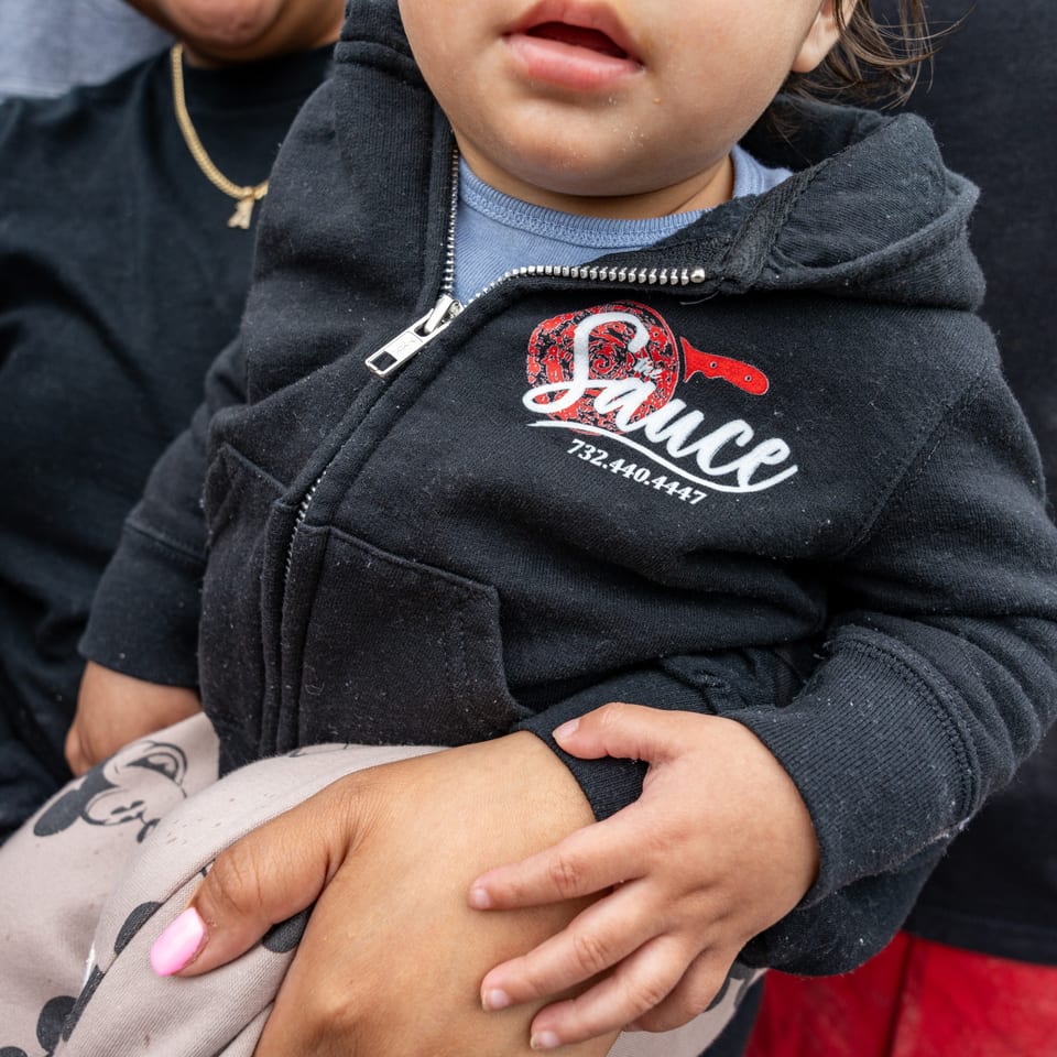 A child wearing a black hoodie with "The Sauce" pizzeria logo and phone number.