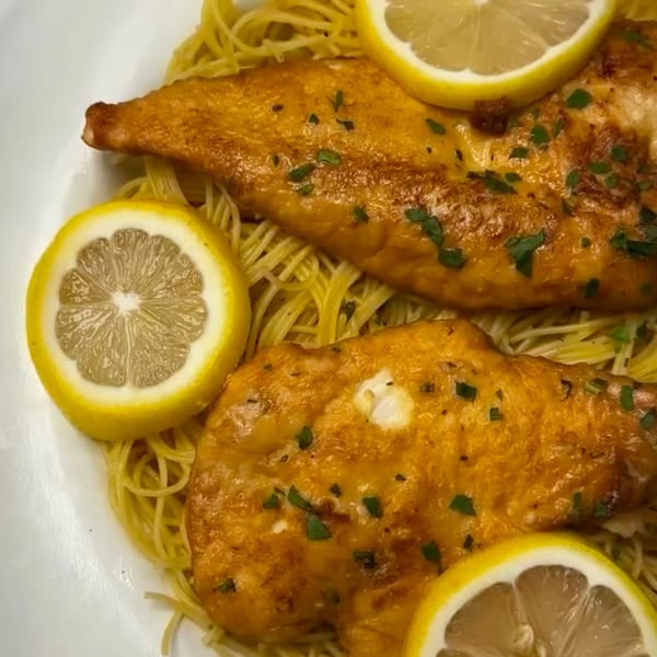 Golden-brown chicken or fish fillets with parsley and lemon slices, served over thin pasta.