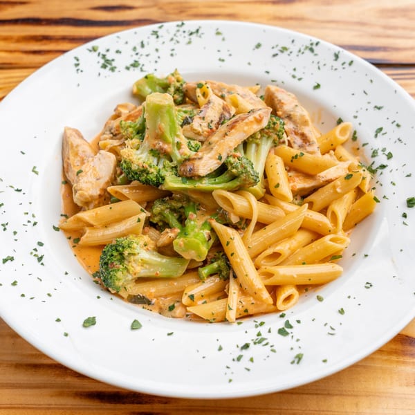 Penne pasta with chicken and broccoli in a creamy sauce, garnished with parsley on a white plate.